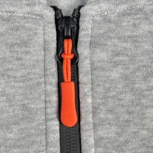 Dettaglio macro della zip nera con cordino arancione su felpa in maglia grigia