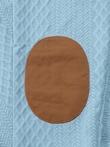 Detail von hellblauem Strickstoff mit geometrischer Textur und braunem ovalem Ellbogen-Patch