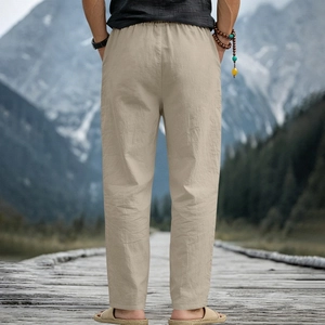Detail of men's linen beach trousers with elastic waist against a scenic lake backdrop