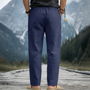 Rear view of men's loose navy linen trousers on a scenic wooden boardwalk and snowy mountain