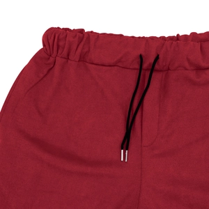 Dettaglio dei jogger rosso scuro con vita elastica e coulisse nere con punte in metallo