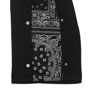 Détail d'un pantalon streetwear noir avec empiècements paisley et boutons-pression argentés