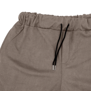Detail view of taupe faux suede pants featuring an elastic drawstring waist and metal tips