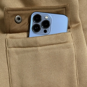 Detail of cargo pocket on camel hoodie with snap button and smartphone inside