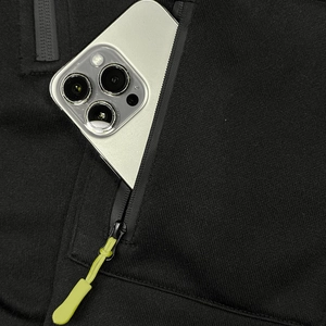 Detail of a functional black hoodie pocket with zipper and neon drawstring holding a phone
