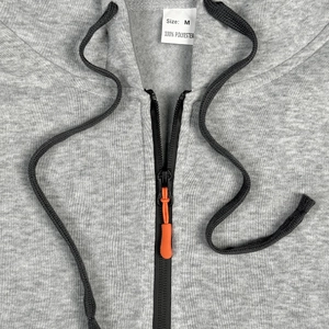 Detail of light gray hoodie with 100% polyester fabric, zipper and orange accents