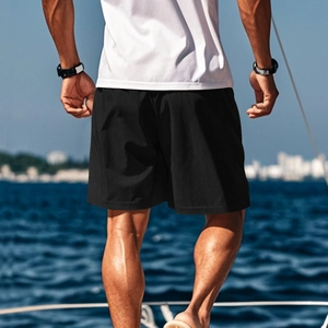 Nahaufnahme schwarzer Mesh-Sportshorts auf Yachtdeck mit blauem Ozeanhintergrund