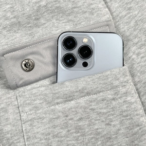 Detail of light grey hoodie pocket with snap button holding a smartphone for scale