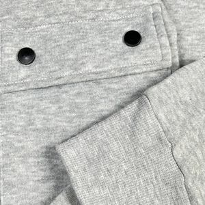 Detail of grey knitted hoodie showing pocket with black buttons and ribbed cuff texture