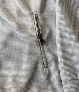 Detailed macro view of light gray waffle knit fabric texture and premium black metal zipper