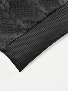 Vista macro del tejido jacquard negro con patrón de hojas y detalle de puño acanalado