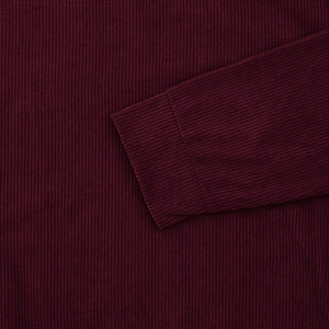 Macro shot of dark burgundy corduroy fabric showing ribbed texture and cuff stitching details