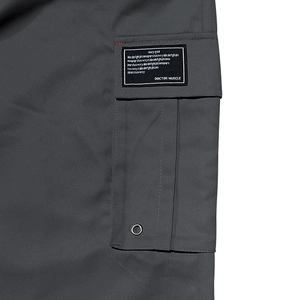 Détail du pantalon cargo gris foncé montrant la poche à rabat et l'étiquette tissée