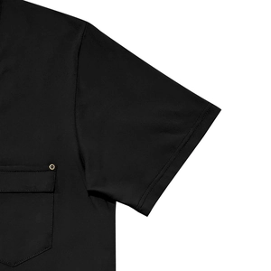 Dettaglio di una camicia nera a maniche corte con taschino sul petto e rivetti metallici