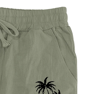 Detail of sage green linen shorts featuring elastic waist, drawstring and palm tree print