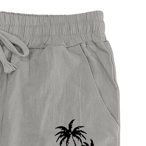 Detail of grey linen trousers featuring elastic waistband and black coconut tree print