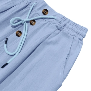 Dettaglio dei pantaloni in lino azzurro con coulisse in vita e bottoni decorativi