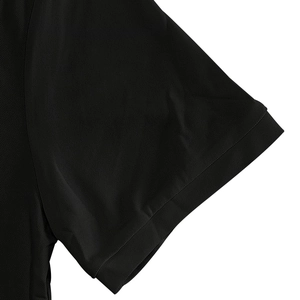 Detailed close-up of the black pique fabric texture and sleeve cuff on this men's polo shirt