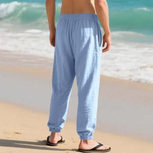 Rear view of men's light blue breathable linen joggers on a bright sunny beach