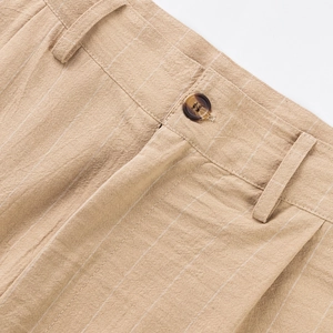 Detailed close-up of khaki striped linen trousers showing texture and amber button