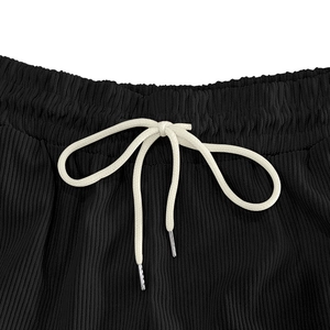 Detail of black corduroy shorts with elastic waistband, drawstring, and metal tips