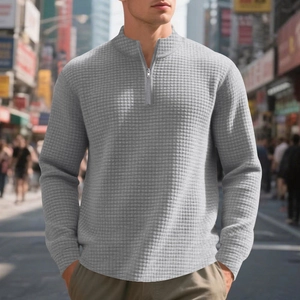 Detail of light gray waffle knit texture on men's quarter-zip pullover in urban setting