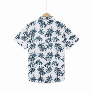 Rear view of a white linen shirt featuring a blue palm tree print on a wooden hanger