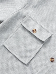 Macro shot of light grey waffle knit fabric with chest pocket and marble-style button