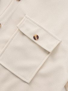 Macro shot of waffle knit texture and a brown tortoiseshell button on cream shirt pocket