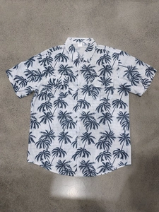 Detailed close-up of a white short sleeve shirt with navy palm tree prints and neck label