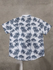 Flat lay back view of Hawaiian shirt showing blue palm tree pattern on textured white fabric