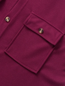 Detail of waffle knit fabric and chest pocket with amber-textured button on wine red shirt