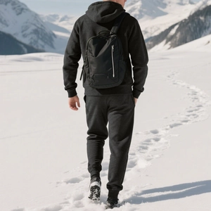 Close-up of a minimalist black outdoor backpack worn by a model in a snowy mountain landscape