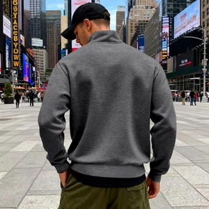Back view of men's dark gray half-zip fleece sweatshirt in an urban city setting