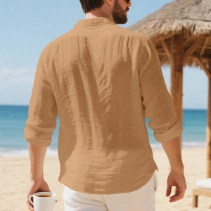 Achteraanzicht van een los linnen herenoverhemd in okerkleur op een zonnig strand