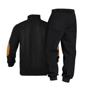 Detail van zwart gebreid pak met contrasterende patches op de ellebogen en de zak