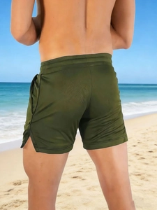 Rear view of dark green quick-dry sports shorts with drawstring and side slits on a beach