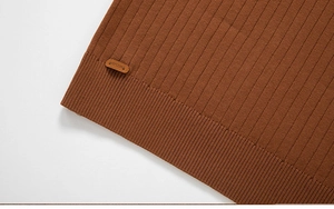 Détail du pull en maille caramel foncé avec ourlet côtelé et étiquette de marque en cuir