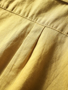 Close-up of mustard linen shirt back detail showing seam stitching and textured fabric