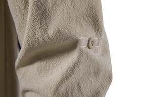Detailopname van de mouwlus met een amberkleurige knoop op het linnen overhemd