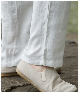 Detail view of white linen pants leg hem and woven canvas loafers in outdoor natural light