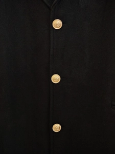 Détail d'un manteau en laine noir montrant trois boutons métalliques dorés gravés
