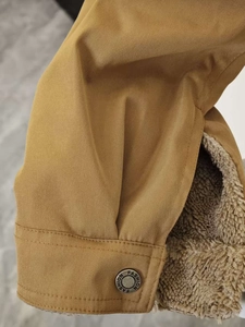 Detail of tan canvas jacket featuring warm fleece lining and branded metal cuff button