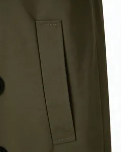 Detail of olive green trench coat showing pocket flap with decorative stitching and matte button