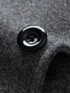 Close-up of a black four-hole button on gray wool overcoat fabric showing fine texture
