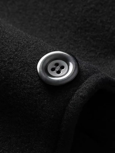 Close-up of a premium round four-hole button on a black wool-blend winter coat fabric