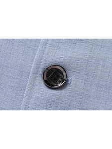Close-up of a black designer button with knight logo on light blue suit fabric texture