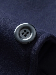 Dettaglio macro di un cappotto di lana blu scuro con un bottone nero in resina lucida