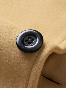 Macro shot of black resin button and camel wool fabric texture on long overcoat
