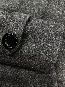Macro della trama di lana grigio scuro e del bottone nero lucido sul polsino del cappotto